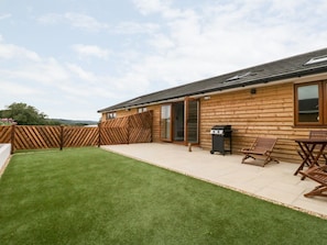 A wooden cabin with a patio, a barbecue grill, and a trash bin. - Honey Bee Retreat, Tytherleigh (Axminster)