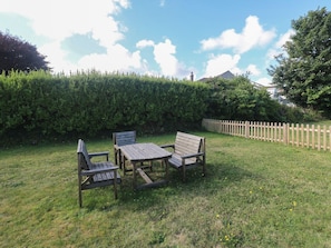 A grassy outdoor area with a wooden table and two chairs, a wooden fence, and a hedge in the background. - 28 Guildford Road, Hayle (Hayle)