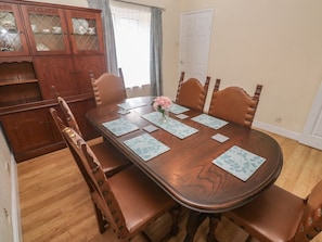A dining table with six chairs, a floral centerpiece, and a wooden cabinet with glass doors. - 28 Guildford Road, Hayle (Hayle)