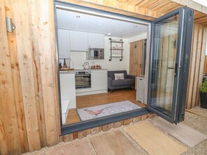 A modern kitchen with white cabinets, a microwave, and a grey sofa. - Hillside Hut is near Ashbourne (Ashbourne)