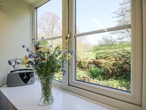 A window with a view of a garden, a radio, and a vase with flowers. - Caradoc Cottage, Church Stretton (Church Stretton)