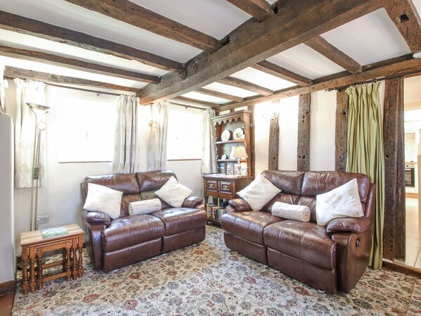 A room with two leather sofas, a wooden side table, a patterned carpet, and a wooden ceiling. - Caradoc Cottage, Church Stretton (Church Stretton)