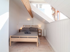 Ein Schlafzimmer mit schrägem Dach, einem hölzernen Bett, Nachttischlampen und einer Heizung.