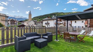 A patio with outdoor furniture, a table, and chairs, surrounded by a wooden fence. - Giuly's Home Luxury Bormio – Alpine Comfort and Wellness (Bormio)