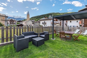 Un patio con mobiliario exterior, una mesa y sillas, rodeado por una valla de madera.