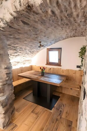Un interior rústico con una zona de estar con banco de madera, una pequeña ventana y una planta en la pared.