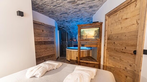 A bedroom with a wooden bed, a wooden wardrobe, and a circular wooden structure with a painting. - Giuly's Home Luxury Bormio – Alpine Comfort and Wellness (Bormio)