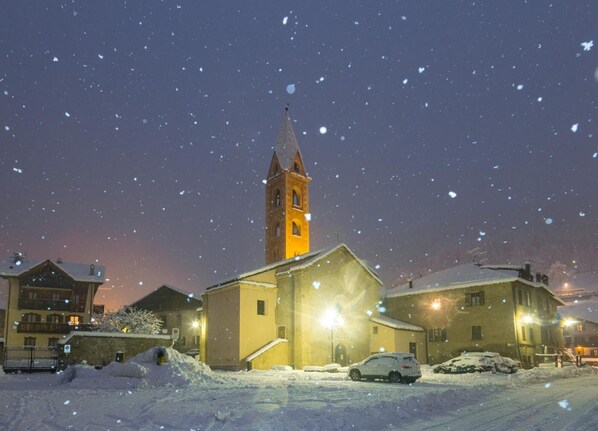 Eine schneebedeckte Kirche mit Glockenturm, umgeben von Wohnhäusern und parkenden Autos.