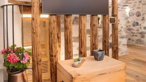 A modern interior with a flat-screen TV mounted on wooden slats, a wooden chest, and a potted plant with pink flowers. - Giuly's Home Luxury Bormio – Alpine Comfort and Wellness (Bormio)