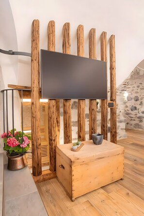 Un interior moderno con un televisor de pantalla plana montado sobre listones de madera, un cofre de madera y una planta en maceta con flores rosas.