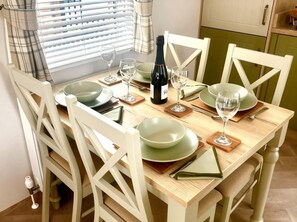 Une table à manger dressée avec des assiettes, des verres et une bouteille, entourée de chaises blanches.