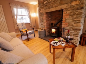 A cozy living room with a stone fireplace, a comfortable sofa, a wicker chair, and a table with food and drinks. - Annie’s Farm Cottage Retreat (Londonderry)