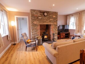 A living room with a stone fireplace, a sofa, a chair, a television, and a lamp. - Annie’s Farm Cottage Retreat (Londonderry)