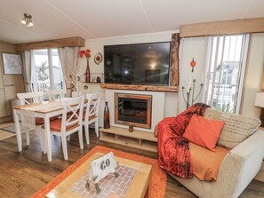 A living room with a fireplace, a TV, a dining area with chairs, and a sofa. - Beachside Retreat in Towyn (Abergele)
