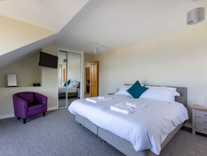 Ein modernes Hotelzimmer mit einem großen Bett, einem violetten Sessel, einem Flachbildfernseher und einem Spiegel.