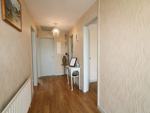 A hallway with wooden flooring, light-colored walls, a white door, and a small table with a vase and picture frame. - Hazel Cottage, Portrush (Portrush)