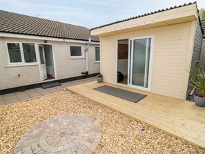 A residential property with a paved patio, a circular brick fire pit, and a wooden deck. - Hazel Cottage, Portrush (Portrush)
