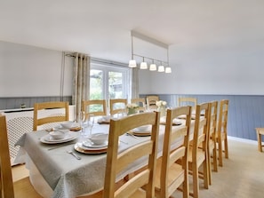 A dining area with a table set for six, wooden chairs, a window with curtains, and a hanging light fixture. - Ingleside: Charming Home in Adsett (Westbury-on-Severn)
