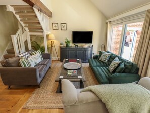 A living room with a staircase, two sofas, a coffee table, a TV, and a window with curtains.