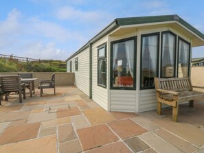 A covered patio area with a seating arrangement, a small table, and a bench. - Cae Carreg, Cemaes Bay (Cemaes Bay)