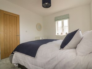 A bedroom with a bed, a wooden door, a window with a valance, and a small bedside table. - 4 Trerammet Crescent, Tintagel (Tintagel)