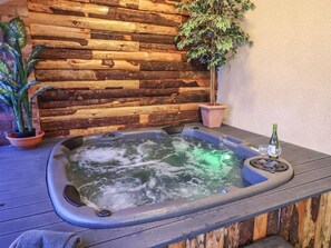 Ein Whirlpool vor einer Holzwand, mit einem Blumentopf und einer Weinflasche.