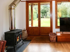 A room with a wood-burning stove, a television, and a large wooden door leading to a garden. - Ringstead Lodge Heacham 4-bed (King's Lynn)