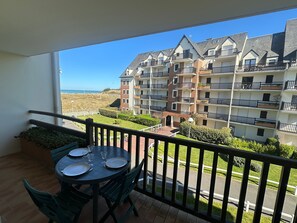 En balkong med ett bord och stolar, med utsikt över ett bostadshus med flera balkonger och fri sikt över havet.