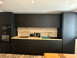 A modern kitchen with dark cabinetry, a wooden countertop, a built-in oven, a coffee maker, and a sink. - Apartment with AC, peaceful - 6 guests (Port-Vendres)