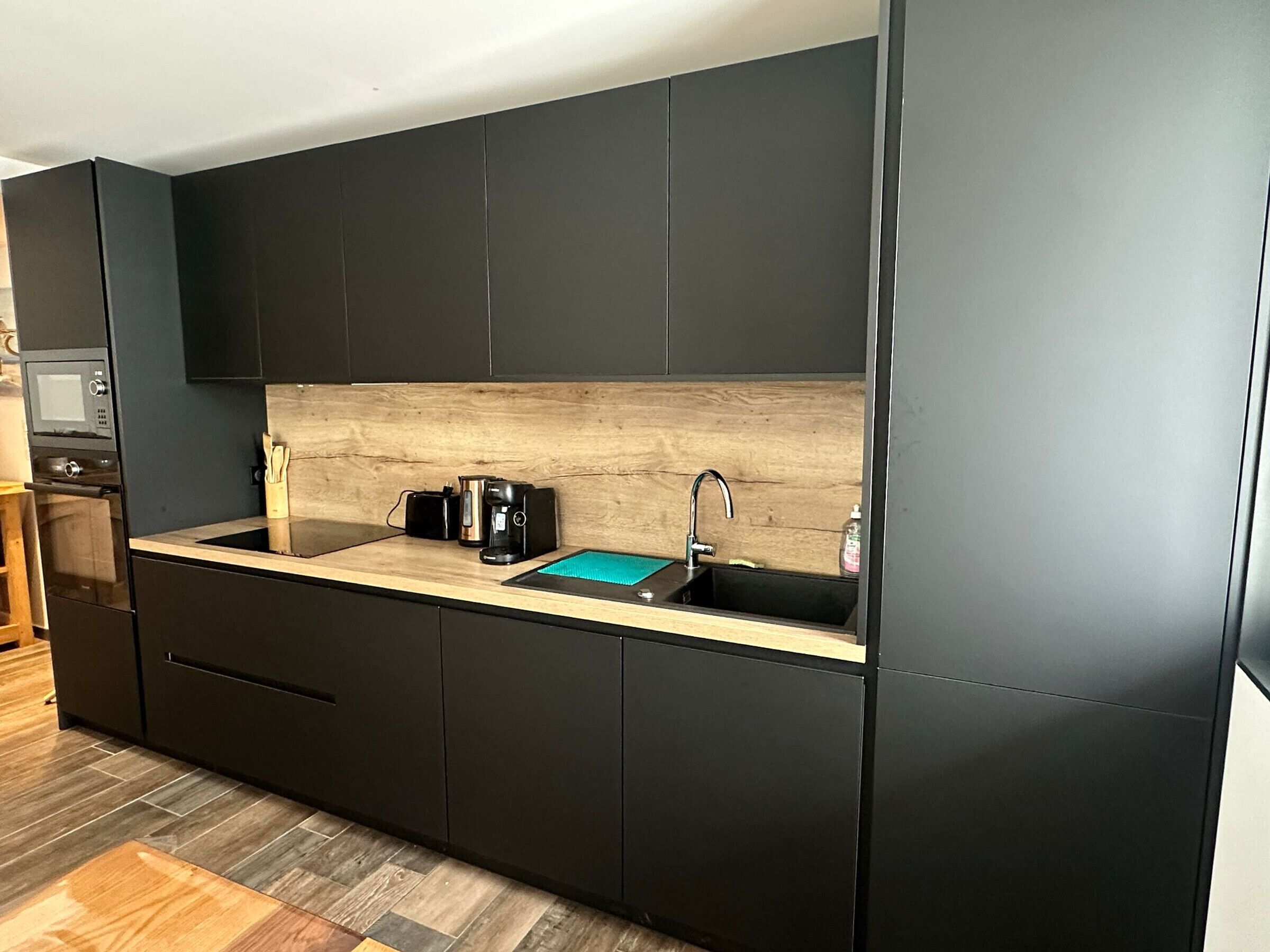 A modern kitchen with dark cabinetry, a wooden countertop, a coffee maker, and a sink.