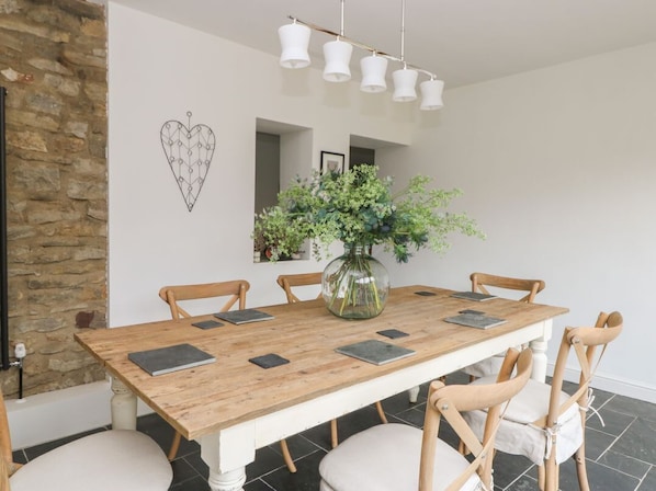 Un comedor con una mesa de madera, seis sillas, un florero con plantas y una lámpara colgante.
