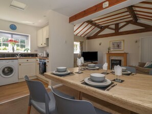Eine moderne Küche mit Holzbalkendecke, ein Essbereich mit Tisch für vier Personen und ein Wohnzimmer mit Kamin.