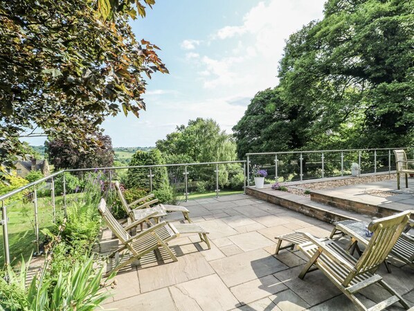 An outdoor patio with wooden chairs and a table, surrounded by a metal railing.