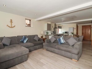 Ein Wohnzimmer mit zwei grauen Sofas, Holzboden, einer Küche im Hintergrund und einer Holztür.