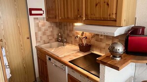 Eine kleine Küche mit Holzausstattung, einer Spüle, einem Geschirrspüler und einem roten Toaster.