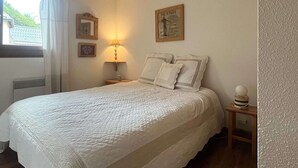 Ein Schlafzimmer mit einem Bett, einer Nachttischlampe, einem Bilderrahmen und einem Fenster mit Vorhängen.