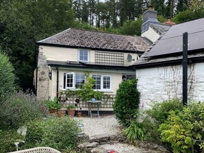 A house with a stone exterior, a tiled roof, and a garden with various plants and a small table.
