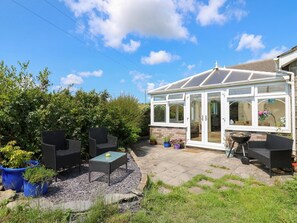 A conservatory with a glass roof, a patio area with outdoor furniture, and a garden with potted plants. - Ty Cariad, St Clears, Smart TV (Carmarthen)