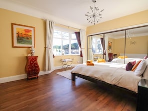 Une chambre à coucher avec un lit, un grand miroir, une fenêtre avec des rideaux, un vase et un tableau au mur.
