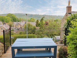 A blue bench on a wooden deck with a metal fence, overlooking a village with houses and greenery. - Ivy Cottage, Winster (Matlock)