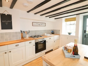 A kitchen with white cabinets, a wooden countertop, a gas stove, and a window with a view. - Ivy Cottage, Winster (Matlock)
