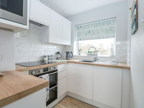 Eine moderne Küche mit weißen Schränken, einer Holz Arbeitsplatte, einem eingebauten Backofen und einem Fenster mit Blick auf Häuser.