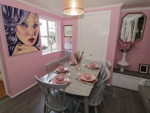 Ein Esszimmer mit rosa Wand, einem großen Gemälde, einer weißen Tür und einem Spiegel.