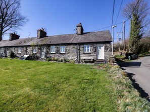 A stone house with a front porch, a small garden, and a clear blue sky. - 1 Bryn Ysgol, Betws-Y-Coed (Betws-y-Coed)