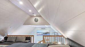 Un dormitorio con techo inclinado, cama con ropa de cama estampada, cabecera de madera, mesita de noche y una obra de arte colgada en la pared.