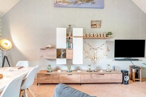 A modern living room with a wooden cabinet, a flat-screen TV, and a dining area with a table and chairs. - Holiday Home 'Galeriehaus Bootsmann' Lake View and Wi-Fi (Stadland)