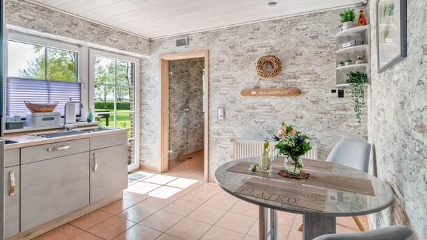Una cocina moderna con encimera de mármol, un comedor con mesa de vidrio y una pared de piedra.