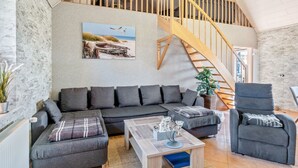 Un espacio habitable tipo loft con una escalera de madera, un sofá gris, una mesa de centro y una planta en maceta.