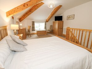 Ein Schlafzimmer mit einem großen Bett, Holzbalkendecke, Fernseher und einem Kleiderschrank.