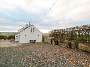 A white building with a sloped roof, a gravel driveway, and a wooden fence. - Moorcrest in Littleham, Devon. (Bideford)